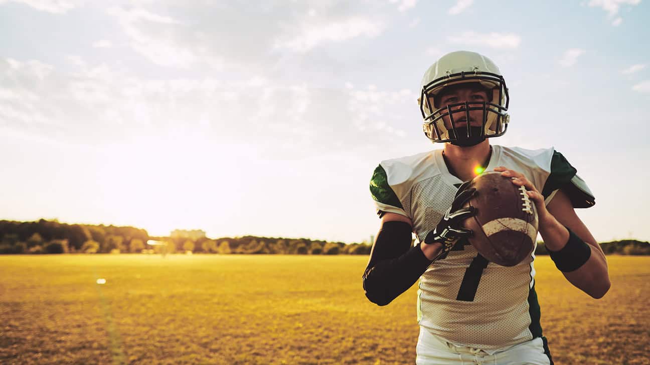 High school football player in full gear holding a football