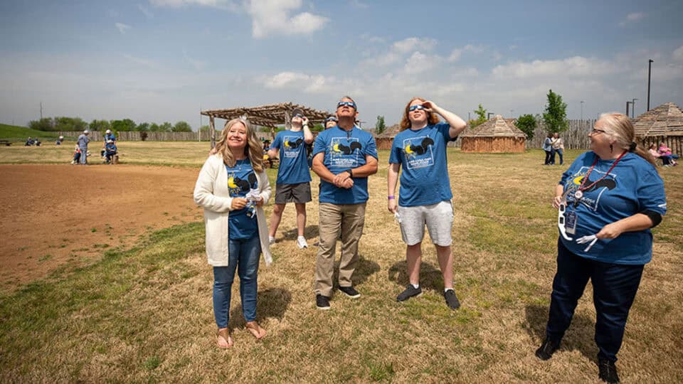 A group of people look at each other and the eclipse in their eclipse glasses