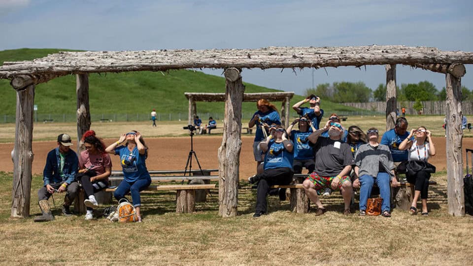 A group of people sit under a pavilion and look at the eclipse