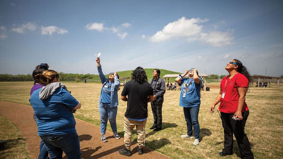 A group of people smile and point while looking at the eclipse