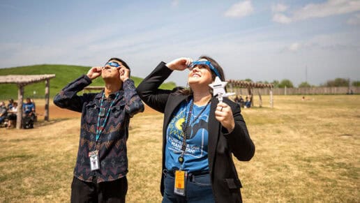 A man and a woman look at the eclipse with their eclipse glasses