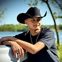 Young man wearing a black cowboy hat, leans on the bed of a truck in front of body of water.