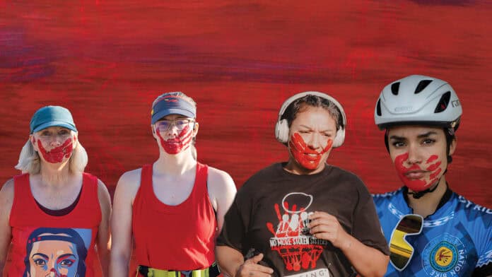 Four women stand together with red face paint on their mouths, representing MMIW