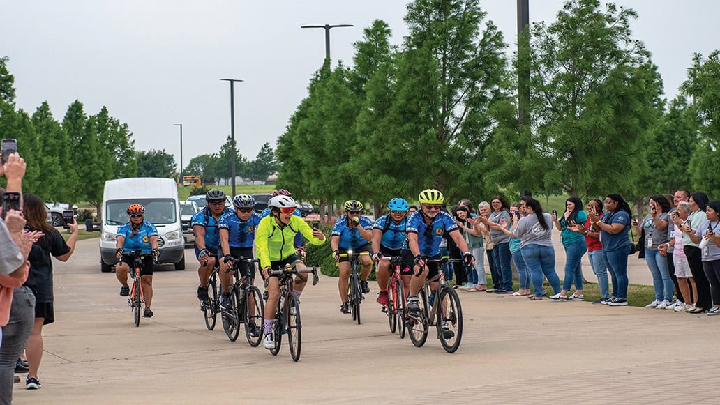 The 2024 Trail of Tears Bike Team rides past lines of fans as they make their way to the Choctaw Nation Headquarters, escorted by Choctaw Lighthorse