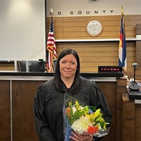 A woman in a black robe holding flowers in front of a judge's bench.