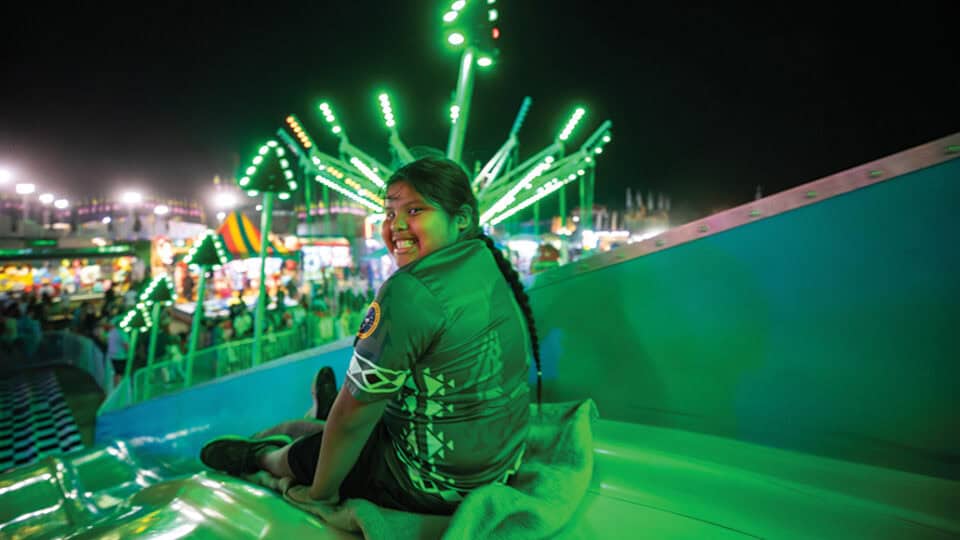 Young girl smiles brightly in the neon green lights as she goes down the slide at Labor Day.