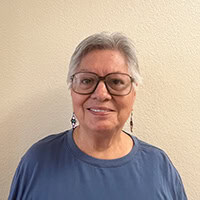 Woman with grey hair and glasses smiles.