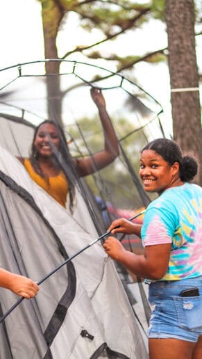 Two girls smile while setting up their tent