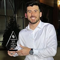 A man in a long-sleeved white shirt holds up a glad trophy while smiling.