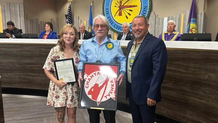 A woman, an older man and council member Anthony Dillard pose for a photo. The man in the middle holds a plaque.