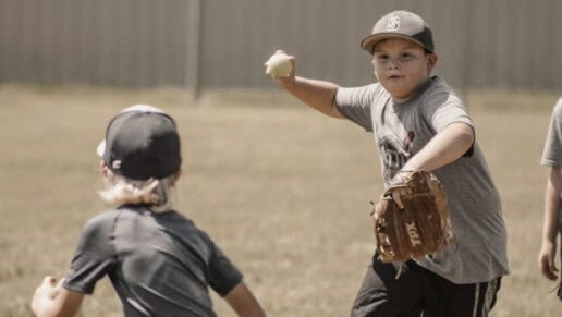 A boy wearing a grey shirt and a baseball hat throws a baseball at a CNO Summer Camp