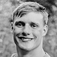 Caden Watson, black and white photo of a young man in a field smiling.