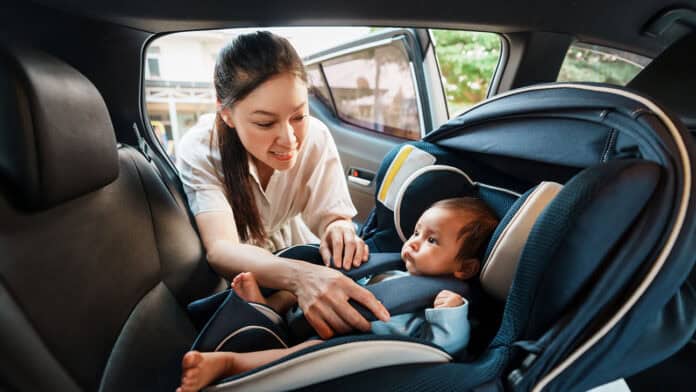 A mother buckles a baby into a car seat