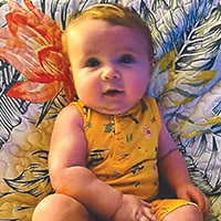 Daxton Countz, a baby in a yellow onesie with green designs on it lays on a floral quilt.