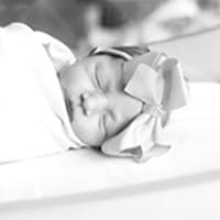 Madeleine Tidmore, black and white photo of a baby wrapped in a blanket with a bow on her head.