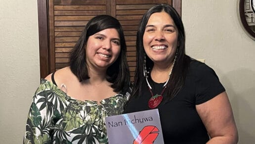 Two women hold up coloring book with a red feather on it.