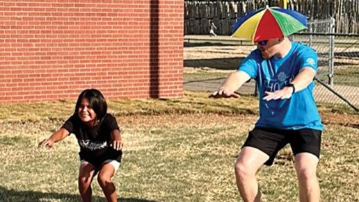 A boy and a man wearing a funny hat do squats.