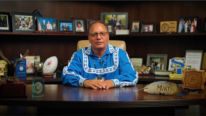 Chief Batton sits at his desk, wearing a blue traditional Choctaw shirt.