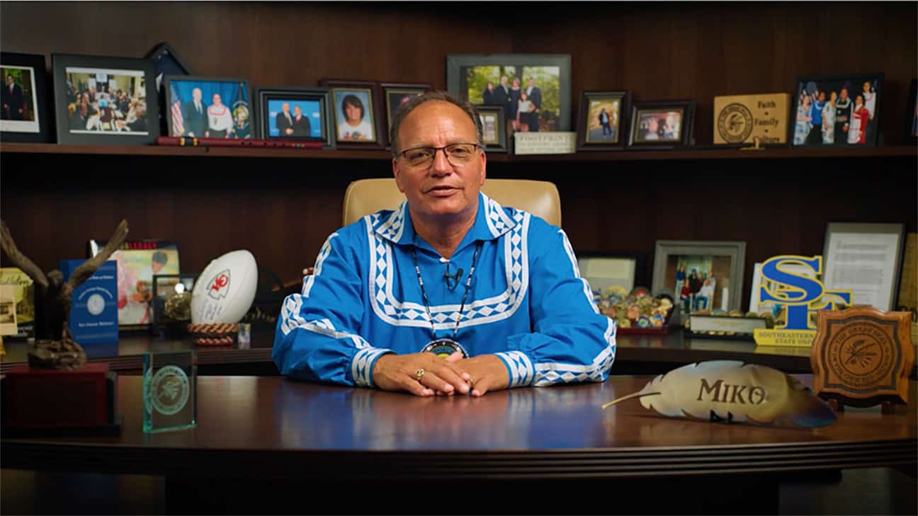 Chief Batton sits at his desk, wearing a blue traditional Choctaw shirt.