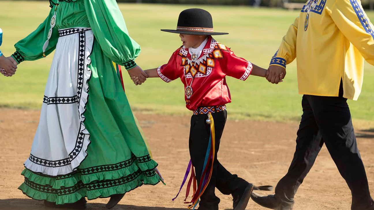 Two adults and child dancing in traditional Choctaw attire