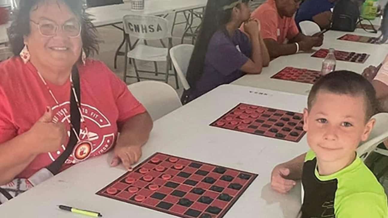 two people pose for teh camera as they play checkers.