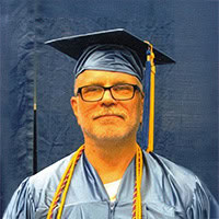 Michael Bingham, a man poses for the camera in his graduation cap and gown.