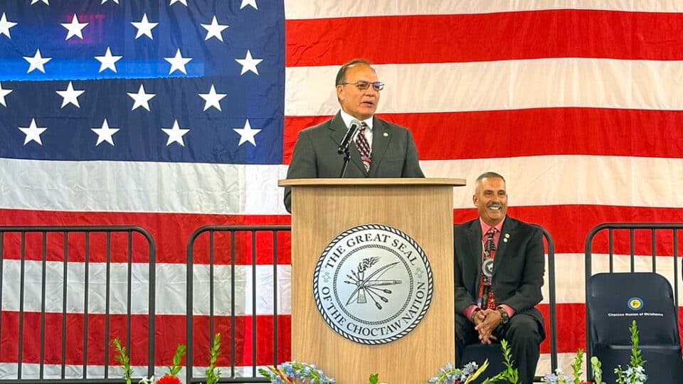 Chief Batton speaks at podium in front of large American flag.