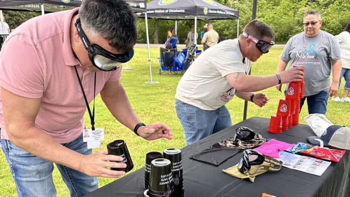 Two men attempt to stack cups while wearing Drunk Buster goggles.