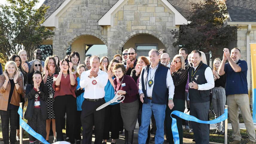 A large group of people applaud as a ribbon is cut for a grand opening.