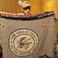 A man in a ballcap holds up Choctaw elder blanket.