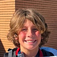 A young man with blond, flowy hair and red cheeks smiles.