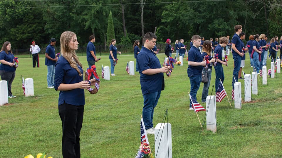 Flags are presented at graves by young adults.