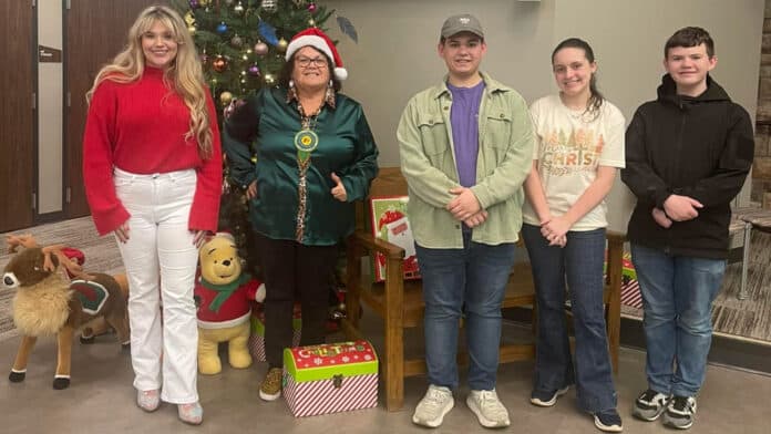 Five people, including, Jennifer Woods, line up for a photo in front of a Christmas tree.