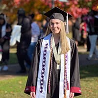 Young woman with blonde hair dressed in graduation cap and gown.