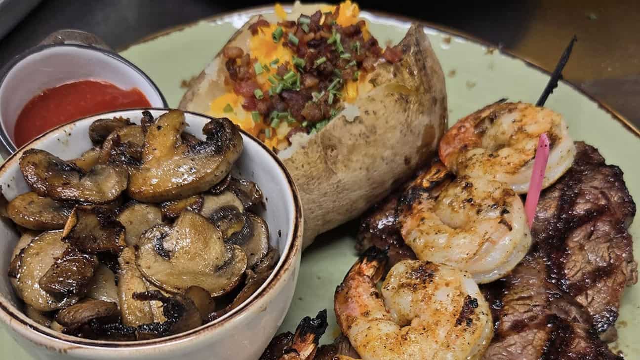 A plate of steak, shrimp, baked potato and mushrooms.